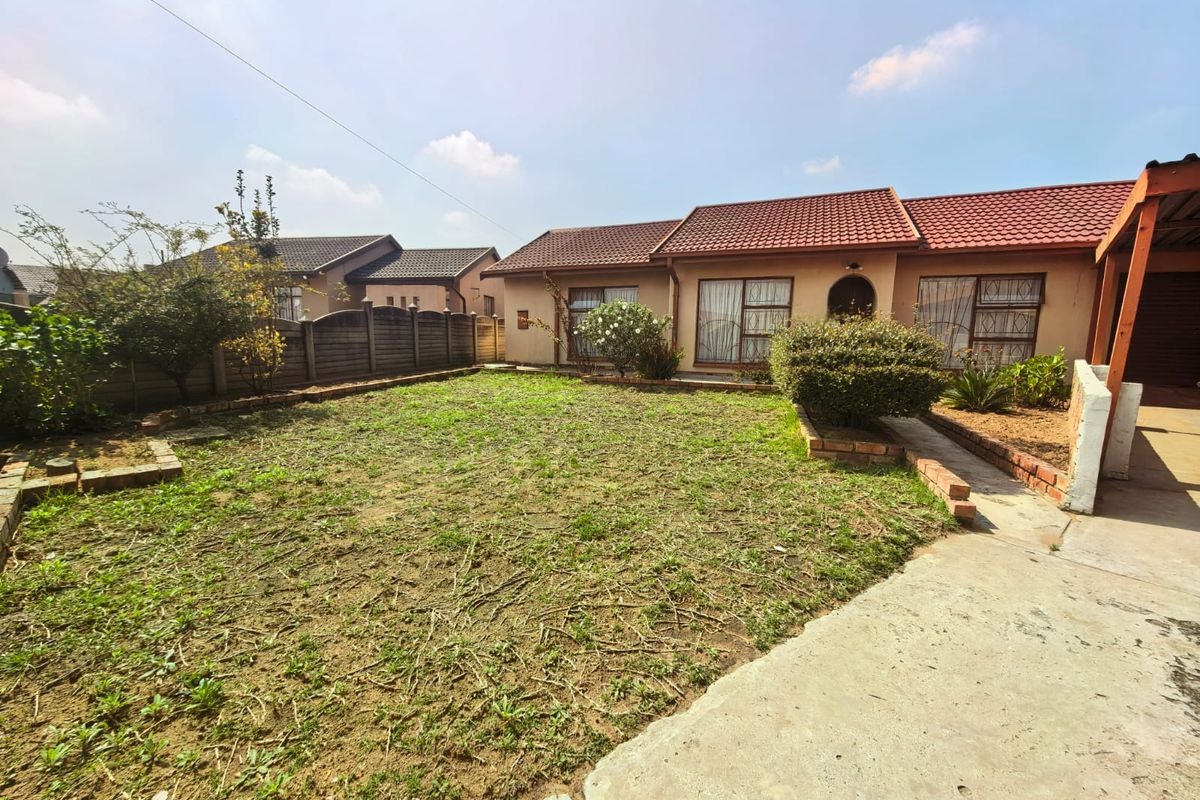 A rear exterior view of the house featuring a tiled roof, security-barred windows, a concrete driveway, and a garden area with brick edging.