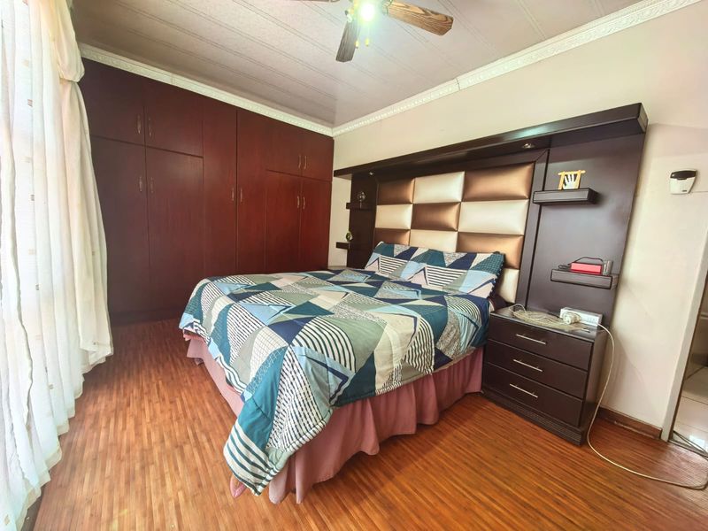 A bedroom featuring laminate flooring, crown molding, a ceiling fan, and extensive built-in cabinetry with an integrated headboard unit.