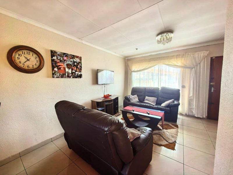 A functional living room featuring tiled flooring and natural light through large windows, providing a comfortable space for relaxation.