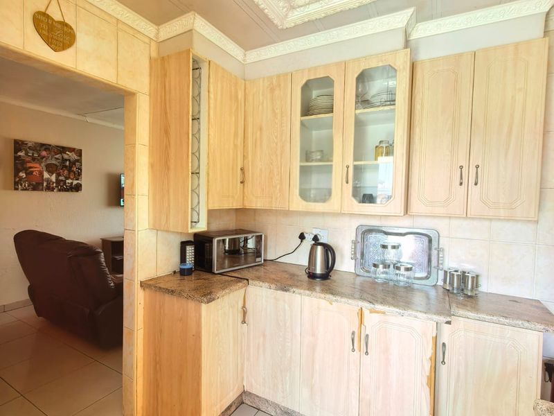 A compact kitchen featuring light wood-tone cabinetry, granite countertops, and decorative ceiling molding, showing signs of wear on the cabinet finishes.