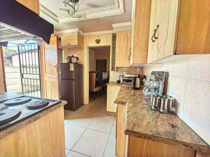 A functional kitchen featuring light wood cabinetry, laminate countertops, tiled flooring, and a built-in electric hob with an overhead extractor fan.