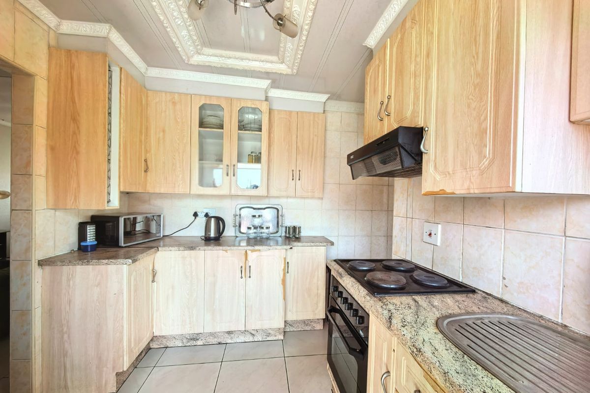 A functional kitchen featuring light wood-finish cabinetry, granite-look laminate countertops, a built-in oven with hob, and tiled flooring throughout.