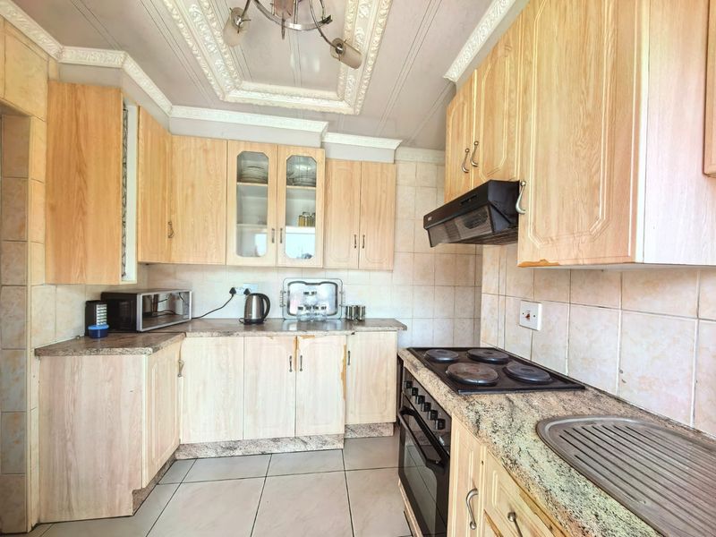 A functional kitchen featuring light wood-finish cabinetry, granite-look laminate countertops, a built-in oven with hob, and tiled flooring throughout.