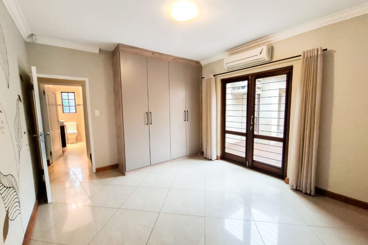 Spacious bedroom featuring neutral tiled flooring, built-in cupboards, an air conditioning unit, and direct access to an outdoor area through double glass doors.