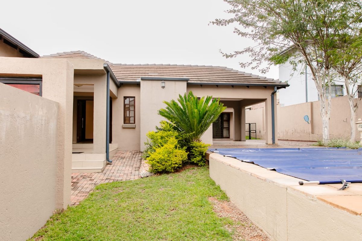 Rear exterior view featuring a swimming pool with cover, paved walkway, and a covered patio area adjacent to the main house structure.