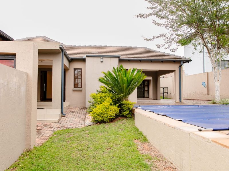 Rear exterior view featuring a swimming pool with cover, paved walkway, and a covered patio area adjacent to the main house structure.