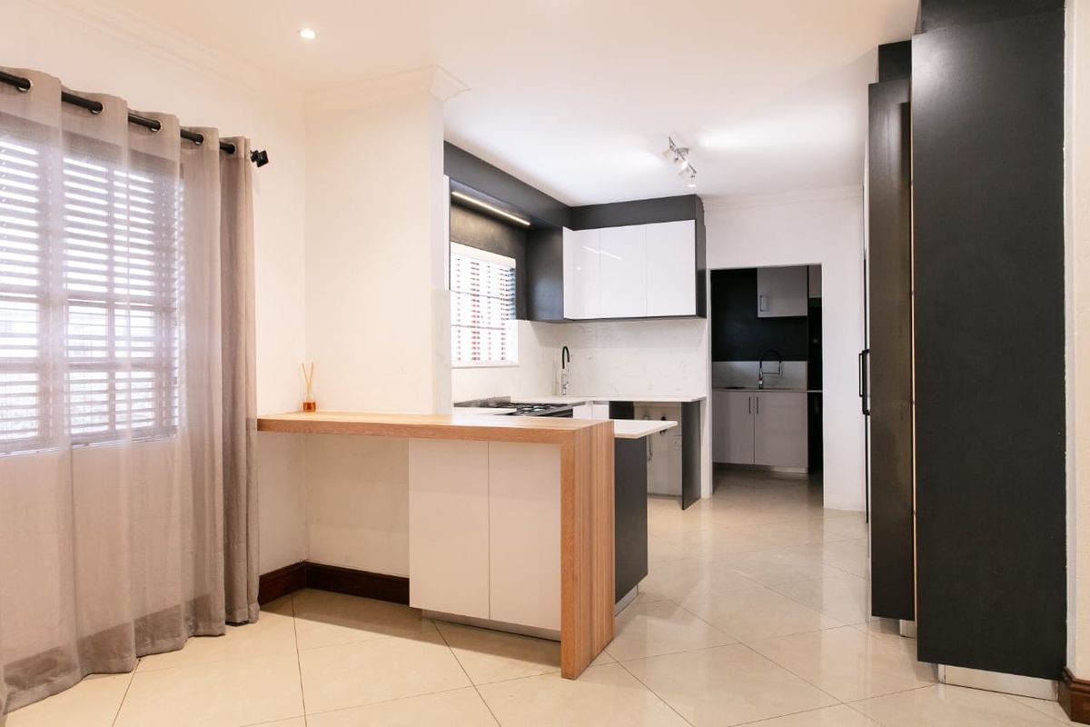 Modern kitchen featuring sleek two-tone cabinetry, stone countertops, a functional breakfast bar, and an adjoining scullery area with tiled flooring throughout.