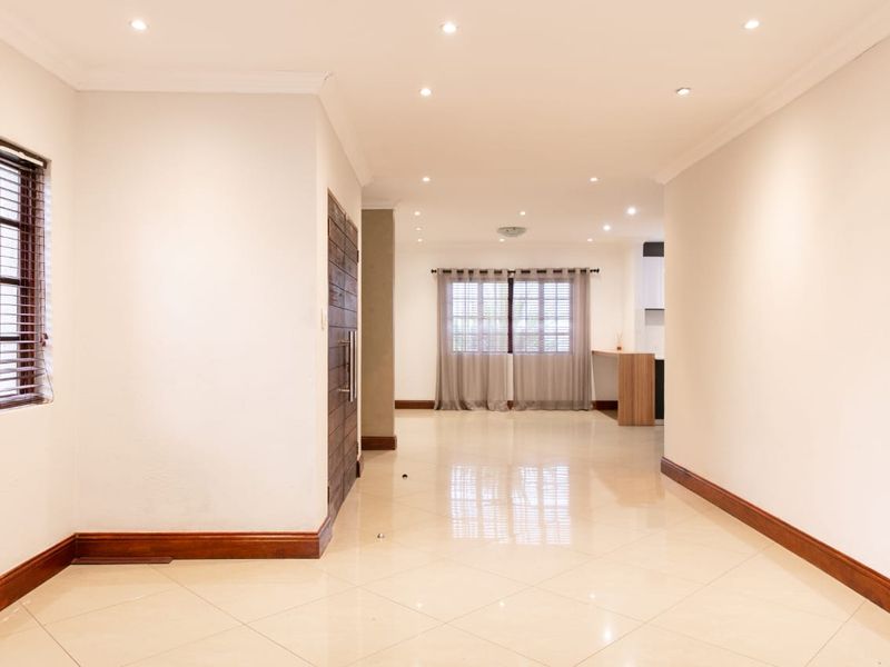 Spacious open-plan living area featuring neutral tiled flooring, recessed downlighting, and timber accents, offering a bright and versatile layout.