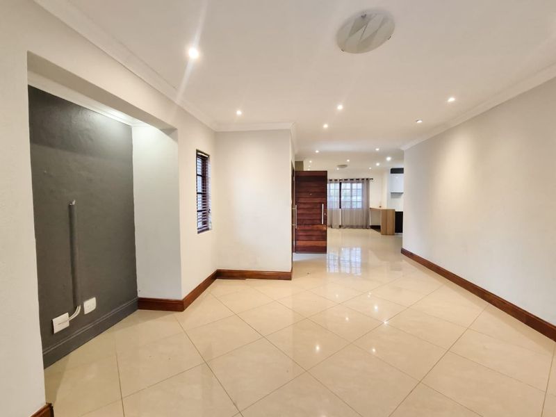 Spacious open-plan living area featuring neutral tiled flooring, recessed downlighting, and a modern flow leading towards the kitchen space.