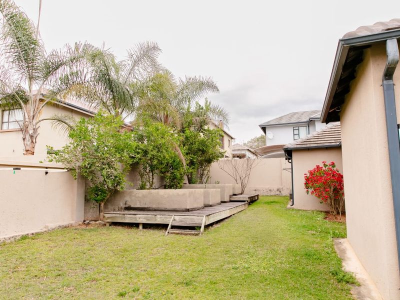 Rear garden area featuring a lawn, raised concrete planters, and a timber deck, enclosed by perimeter boundary walls.