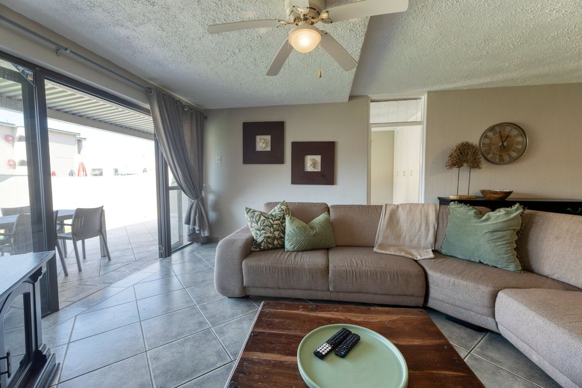 A comfortable living room featuring tiled flooring, a ceiling fan, and large sliding glass doors that provide direct access to an outdoor patio area.