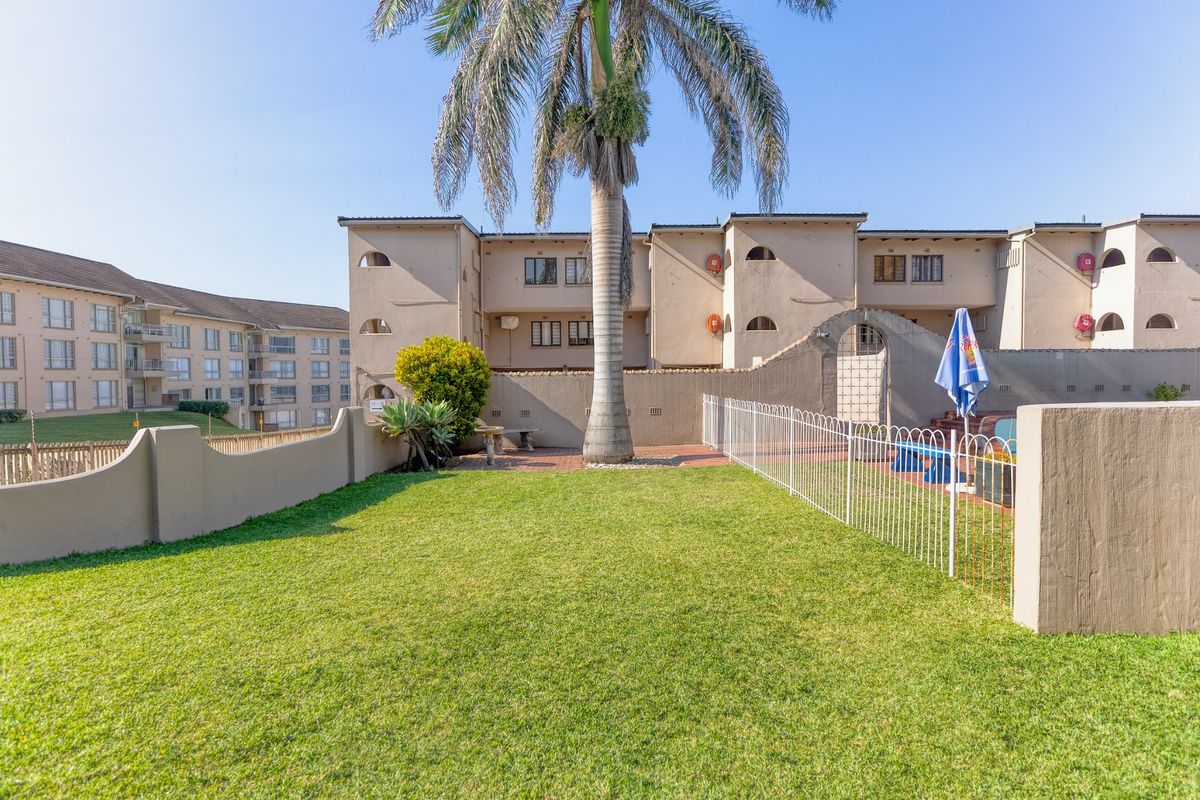 A well-maintained rear garden area featuring a manicured lawn, paved section, and secure perimeter fencing within an apartment complex setting.