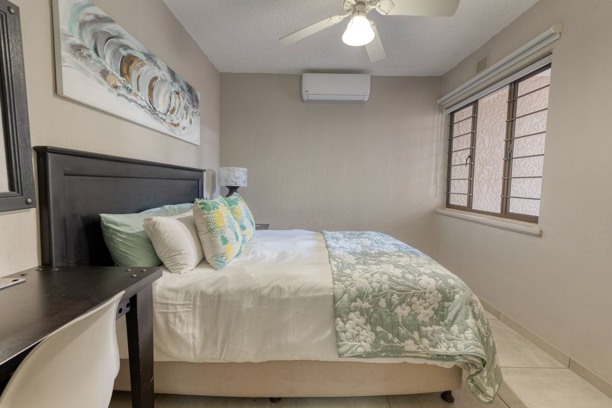 A well-maintained bedroom featuring tiled flooring, a ceiling fan, and a wall-mounted split-system air conditioner for climate control.