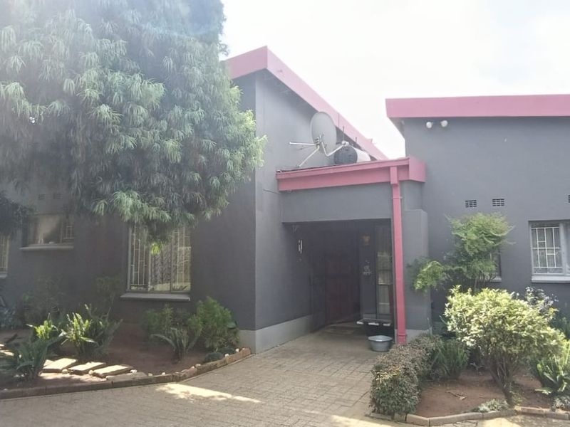 Front elevation of a residential property featuring a paved entrance, grey exterior walls with contrasting trim, and established garden landscaping.