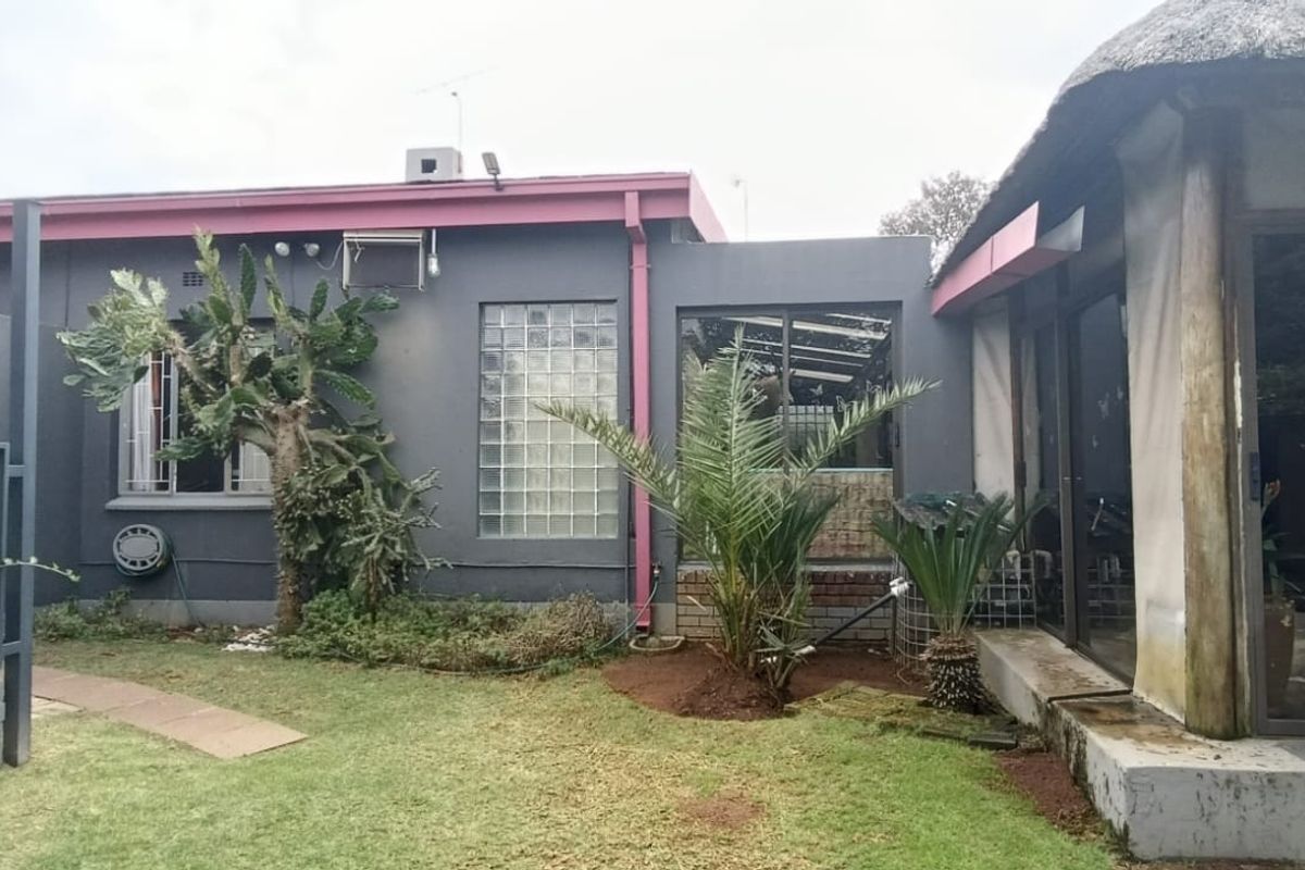 Rear exterior view of the property featuring a lawn, a section with a thatched roof, and a glass block window.