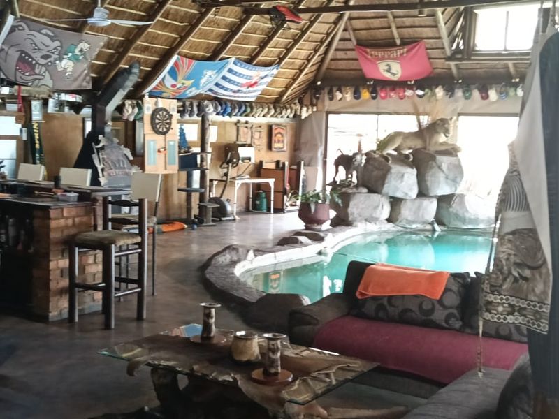 Unique indoor entertainment area featuring a built-in swimming pool, thatched roof with exposed timber beams, and a rustic brick bar counter.
