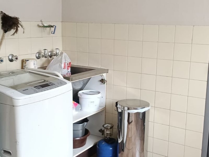 A functional laundry area featuring a stainless steel sink, tiled splashback, and a secure metal gate entrance.