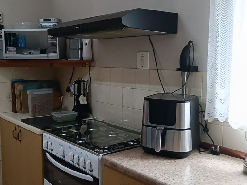 A functional kitchen area featuring a gas stove, oven, extractor fan, tiled backsplash, and laminate countertops with built-in cabinetry.