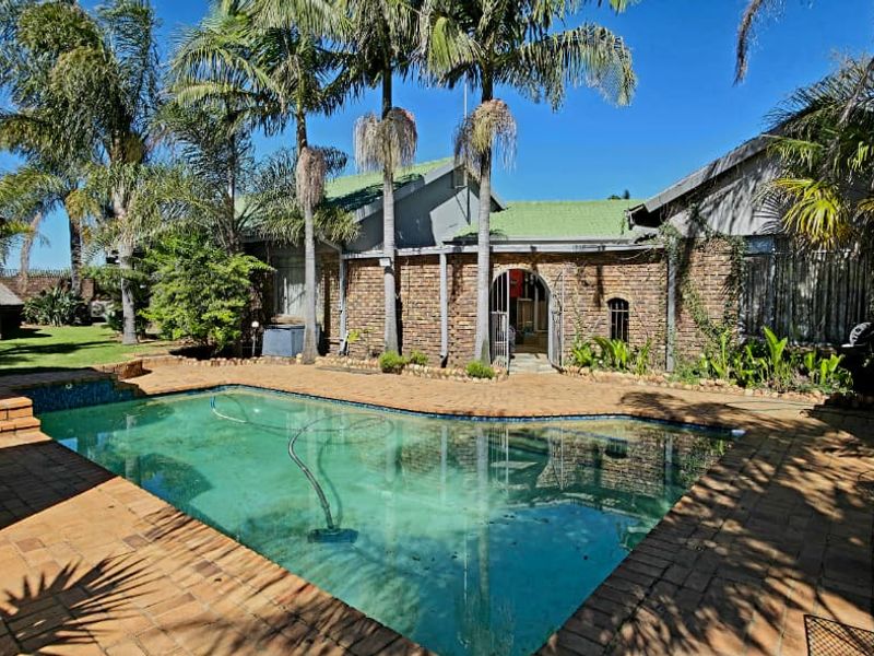 A rear garden area featuring a swimming pool, brick paved surround, and established palm trees set against a brick house facade.