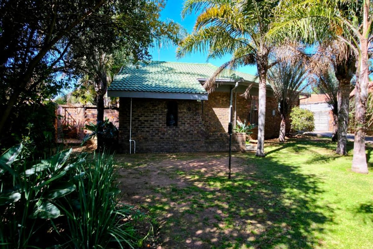 A view of the rear face brick facade of the house, featuring a mature garden with established trees and lawn.