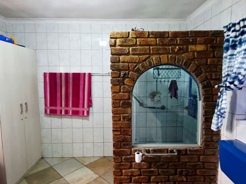 A bathroom featuring a unique brick partition wall, fully tiled surfaces, and a functional layout with standard sanitary fixtures.