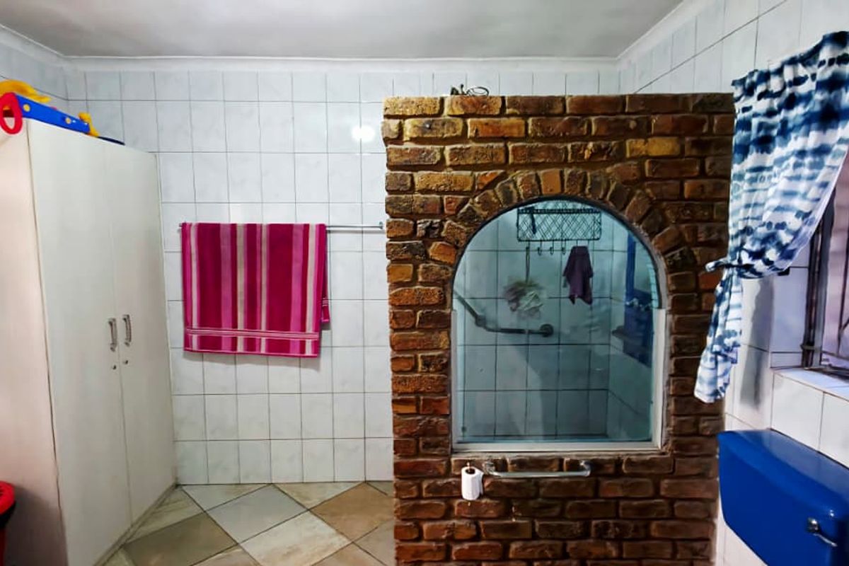 A bathroom featuring a unique brick partition wall, fully tiled surfaces, and a functional layout with standard sanitary fixtures.