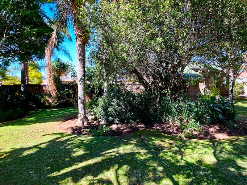 A well-maintained, lush garden featuring mature trees, established landscaping, and a brick boundary wall providing privacy.