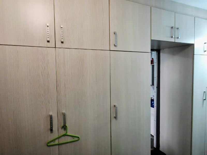 A bedroom featuring extensive light wood-grain built-in cupboards with overhead storage units, providing ample integrated storage space.
