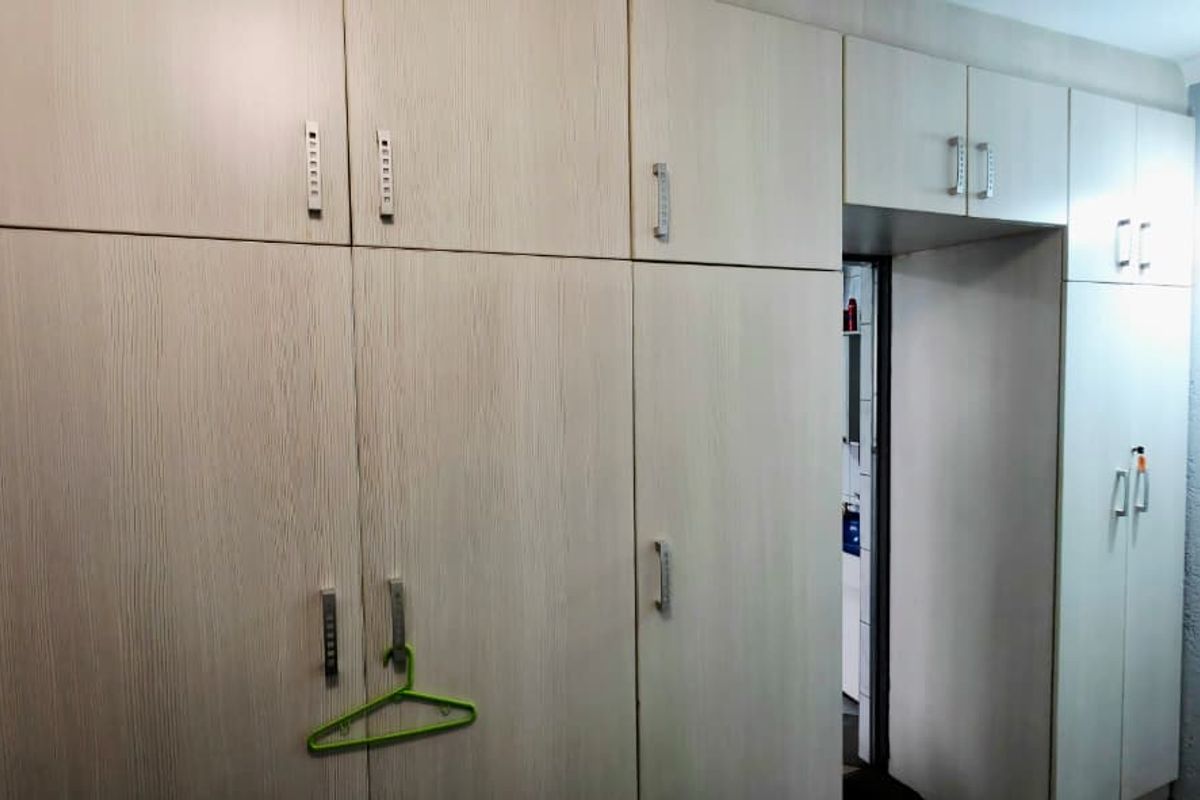 A bedroom featuring extensive light wood-grain built-in cupboards with overhead storage units, providing ample integrated storage space.