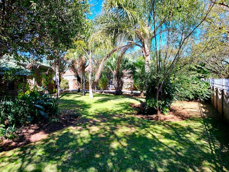 A spacious, established garden featuring mature trees, a well-maintained lawn, and secure perimeter boundary walling with metal fencing.