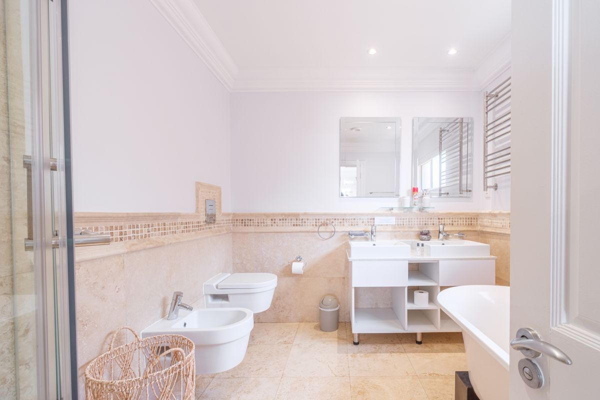 A well-appointed bathroom featuring a double vanity, freestanding bathtub, wall-mounted toilet, bidet, and heated towel rail with elegant stone tiling throughout.