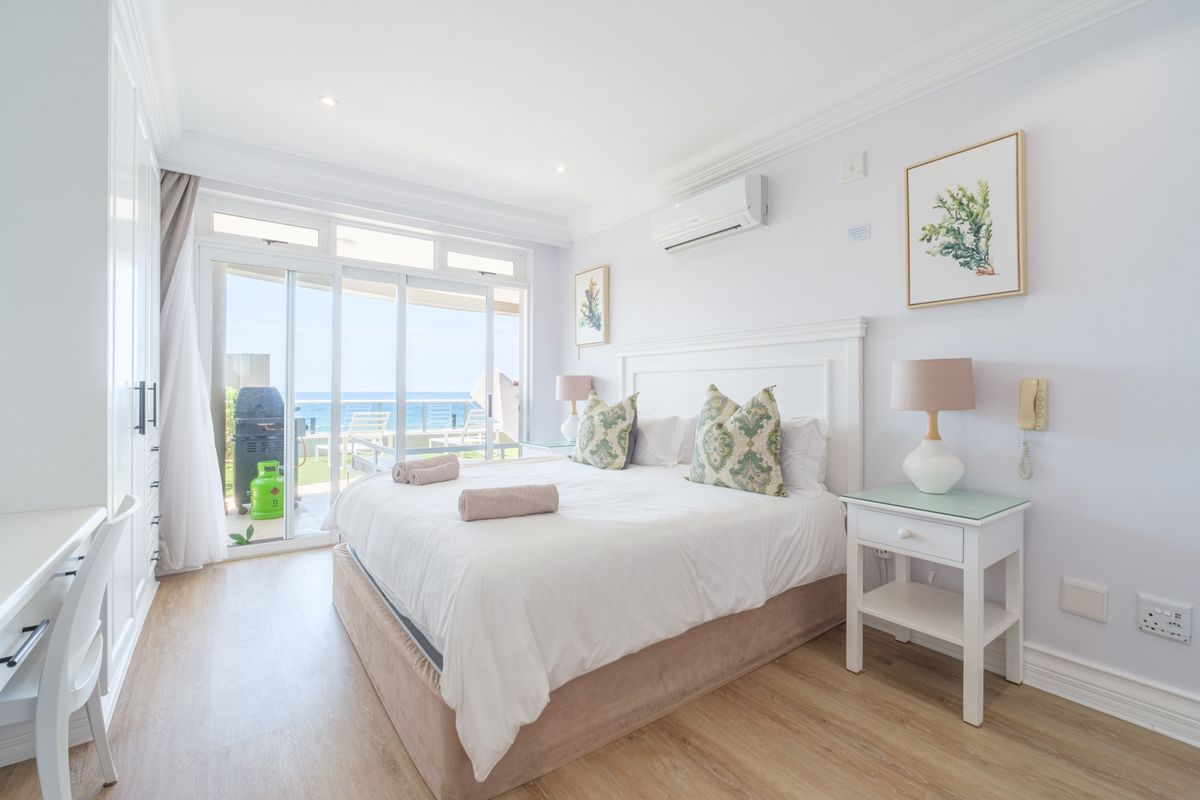 Bright bedroom featuring laminate flooring, built-in cupboards, and sliding glass doors opening to a balcony with ocean views.