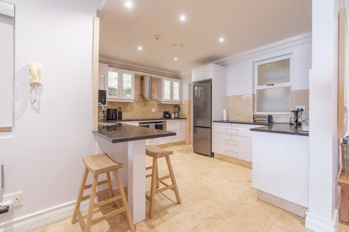 A well-maintained kitchen featuring granite countertops, white cabinetry, stone tile flooring, and a breakfast bar, illuminated by recessed ceiling lighting.