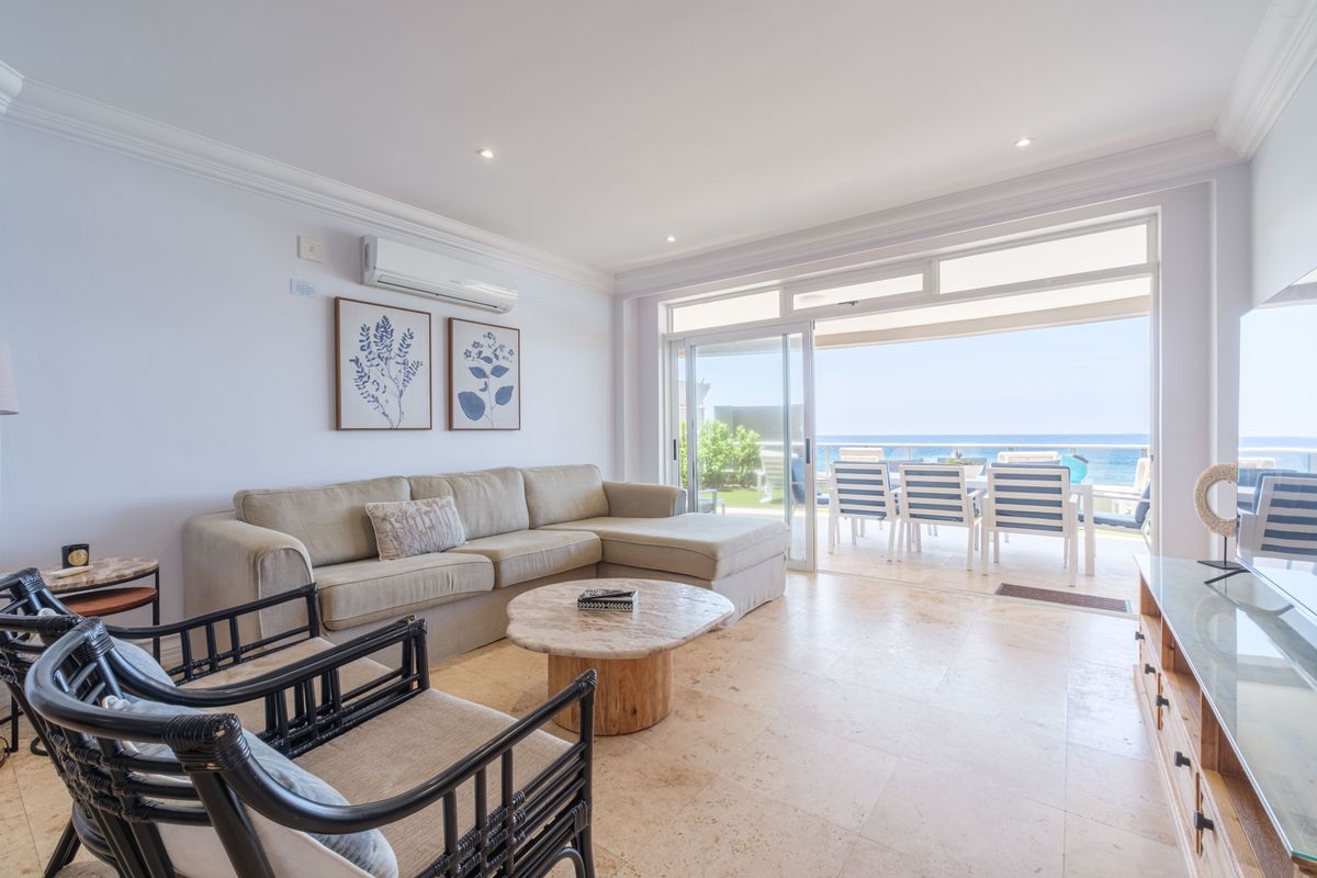 Bright and airy living room featuring stone tile flooring, recessed lighting, and large sliding glass doors that open to a scenic ocean-view balcony.