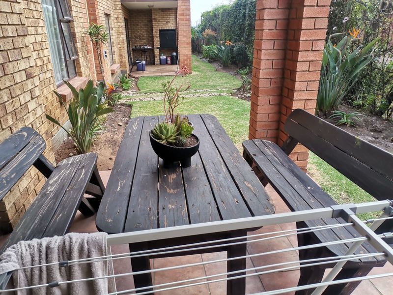 A covered brick patio area featuring tiled flooring and a built-in braai, overlooking a private garden space.
