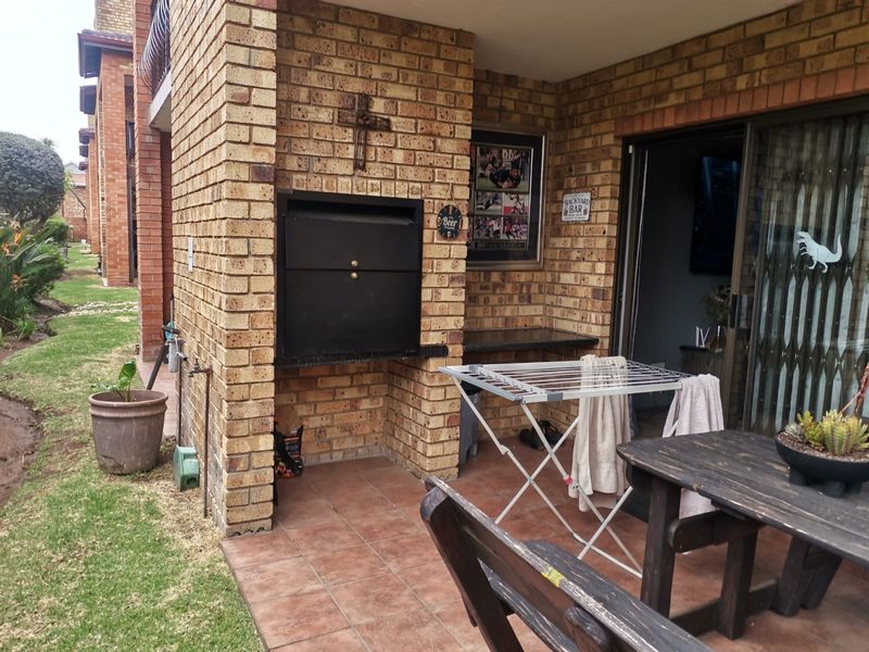 Covered patio area featuring a built-in braai, granite prep surface, and tiled flooring, providing direct access to the interior living space.