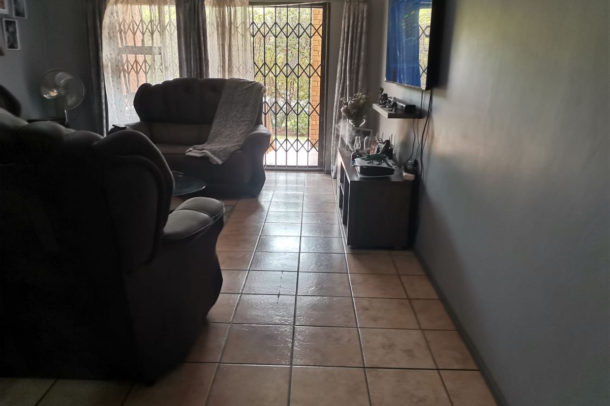 A living room featuring tiled flooring and a sliding glass door with a security gate leading to the exterior.