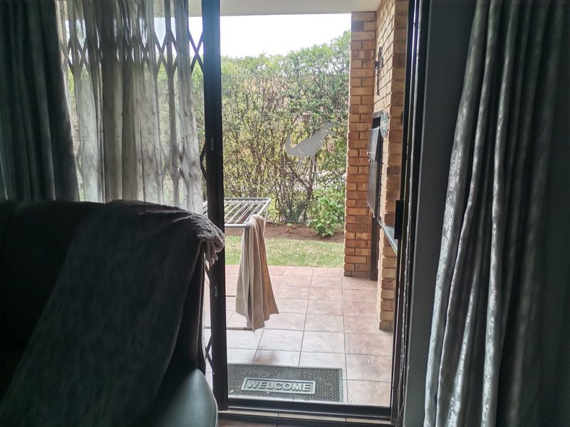 A covered patio area featuring tiled flooring, a brick wall, and a built-in braai, accessible through a sliding door with a security gate.