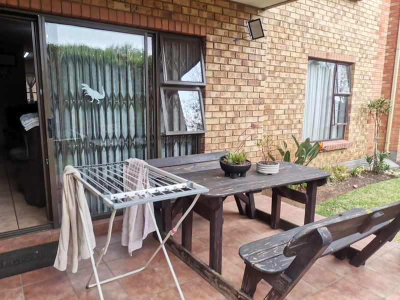 A paved outdoor patio area featuring brick wall construction, sliding glass doors with security gates, and external lighting, providing direct access to the apartment interior.