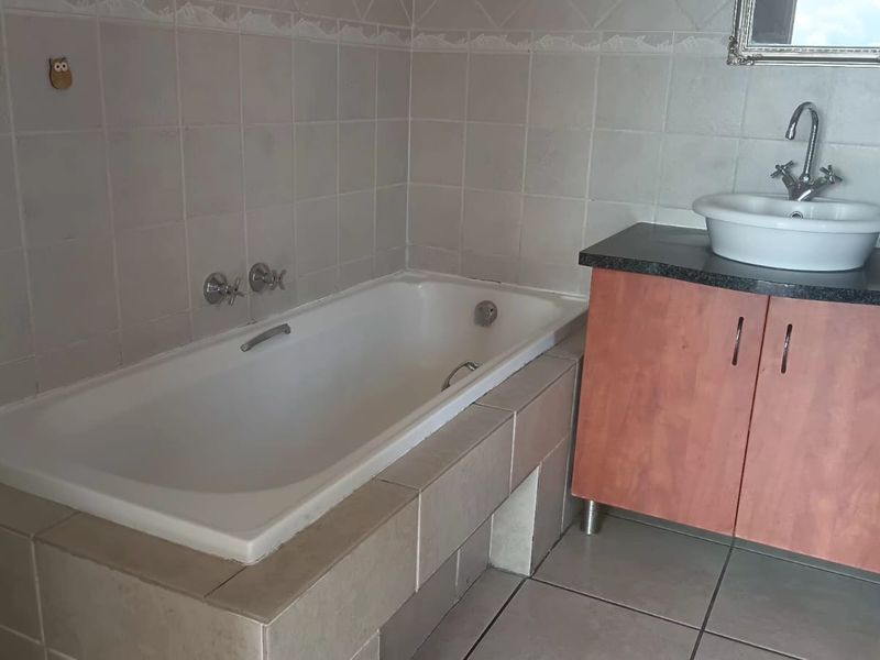 A functional bathroom featuring a built-in bathtub, a vanity cabinet with a countertop basin, and neutral wall and floor tiling.