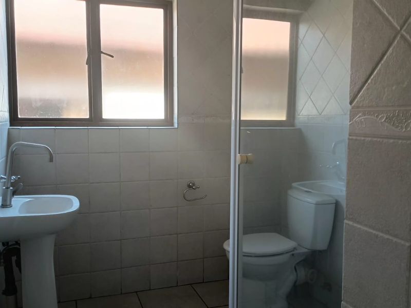A functional bathroom featuring a pedestal basin, toilet, and a glass-enclosed shower with tiled walls and flooring.
