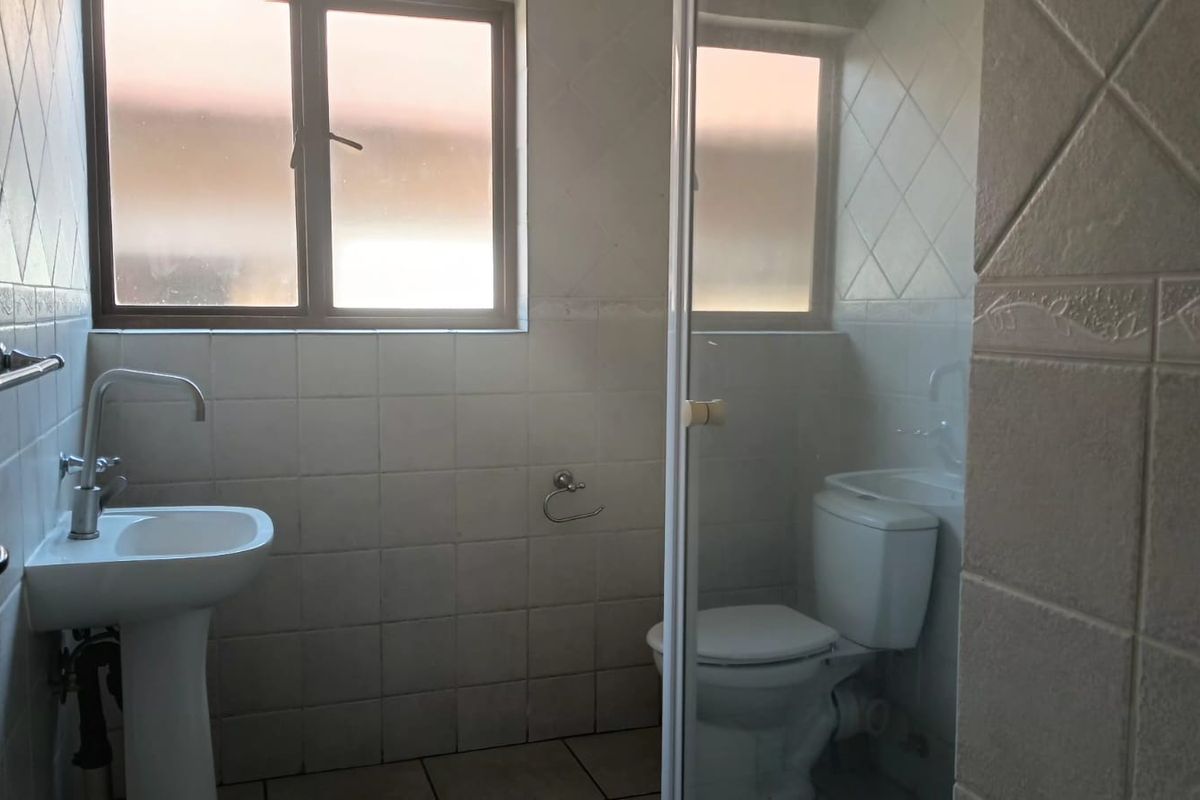 A functional bathroom featuring a pedestal basin, toilet, and a glass-enclosed shower with tiled walls and flooring.