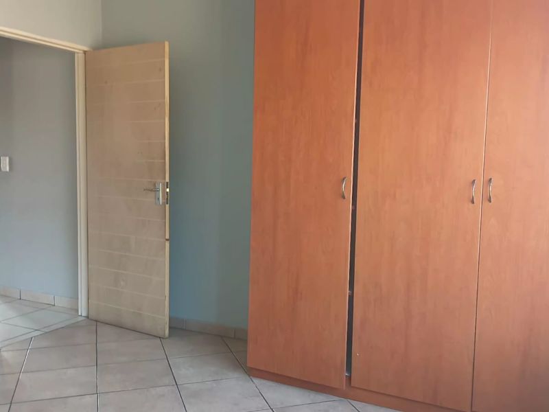 A bedroom featuring tiled flooring and a large built-in wooden wardrobe, providing ample storage space within the room.
