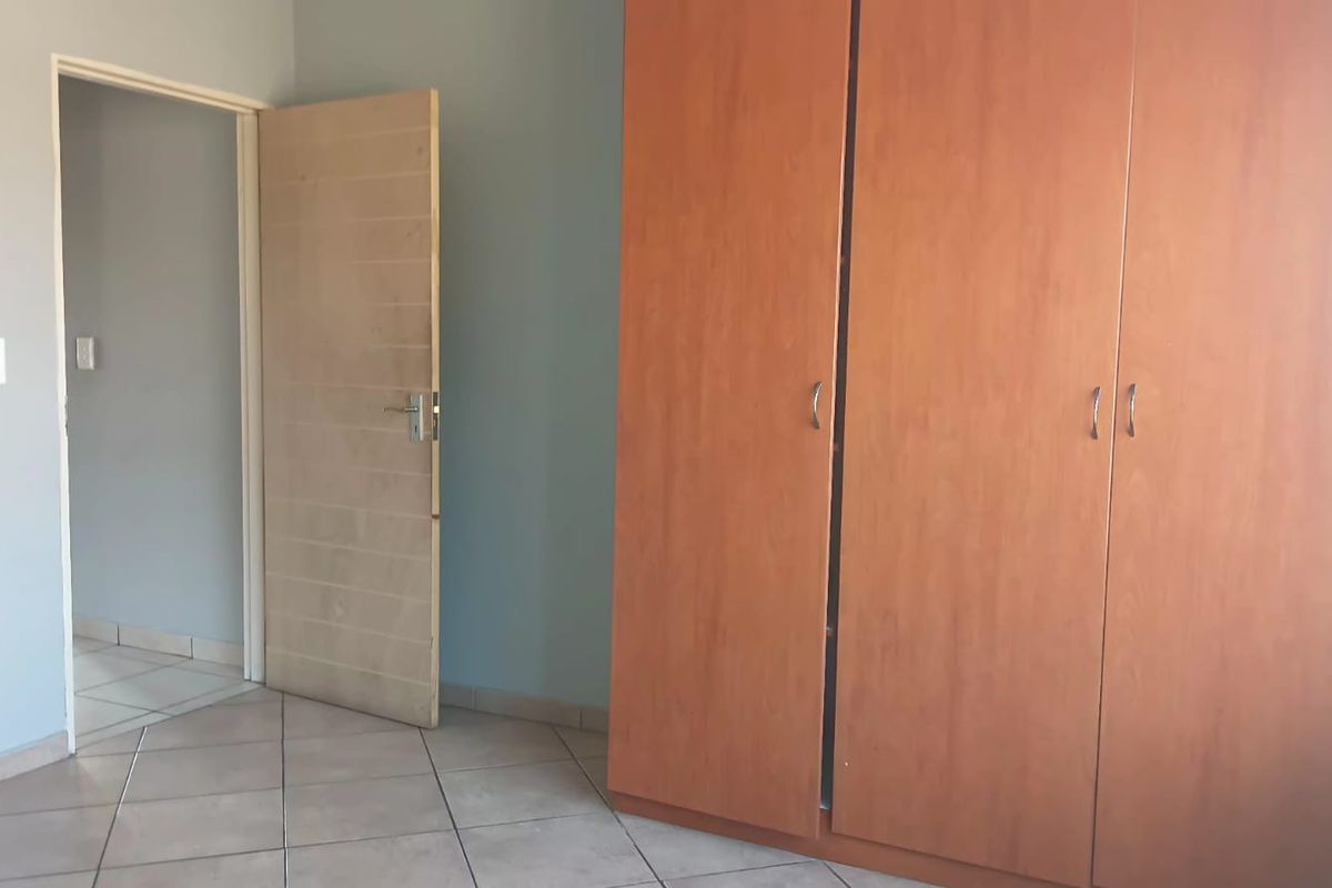 A bedroom featuring tiled flooring and a large built-in wooden wardrobe, providing ample storage space within the room.