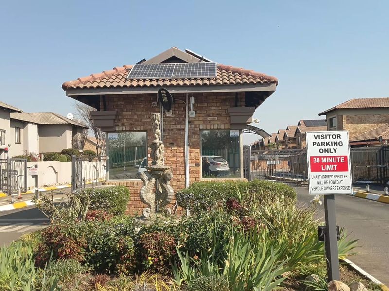 The entrance to the apartment complex features a brick guardhouse with solar panels, secure gated access, and landscaped surroundings.