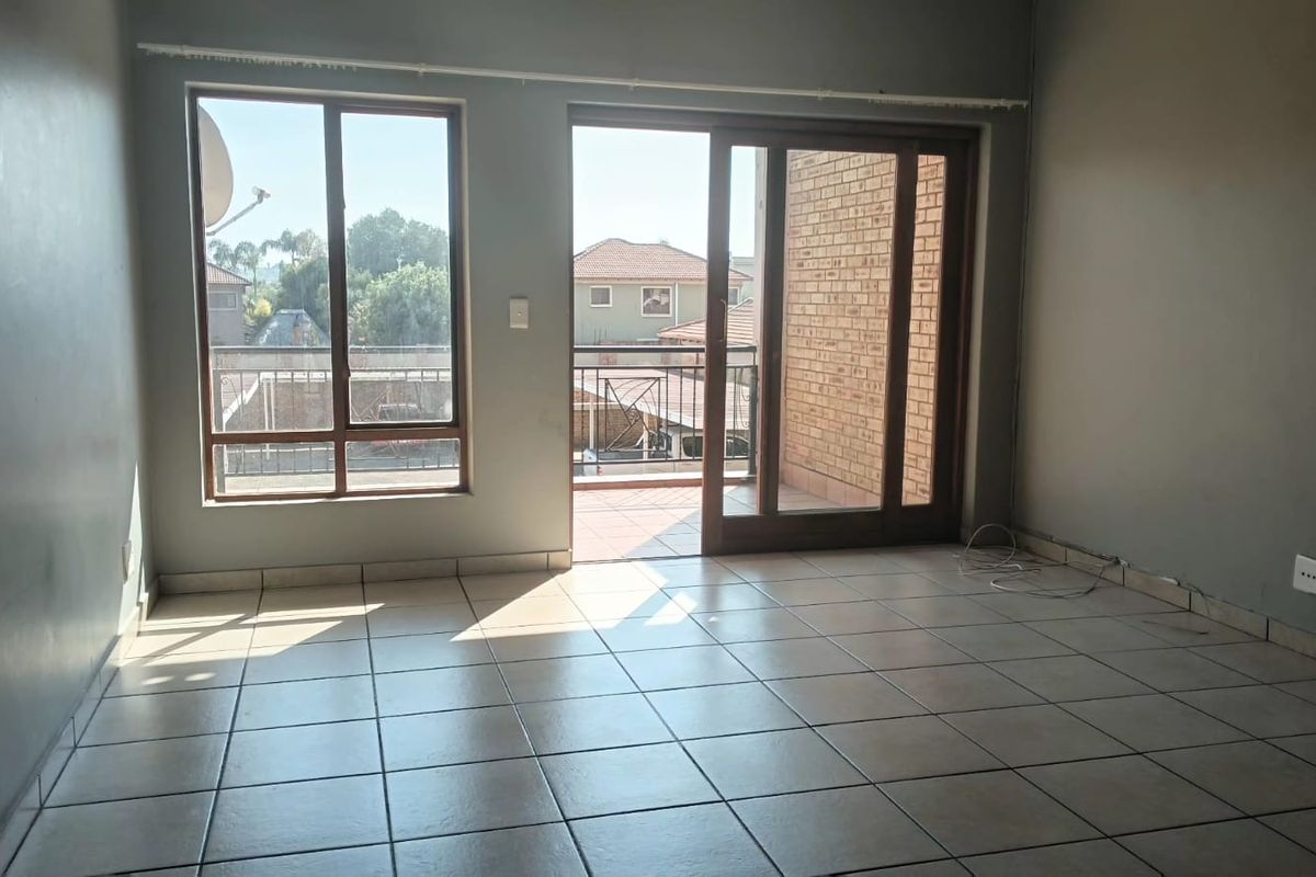 An empty living room featuring tiled flooring, large windows, and a sliding glass door providing access to an outdoor balcony area.
