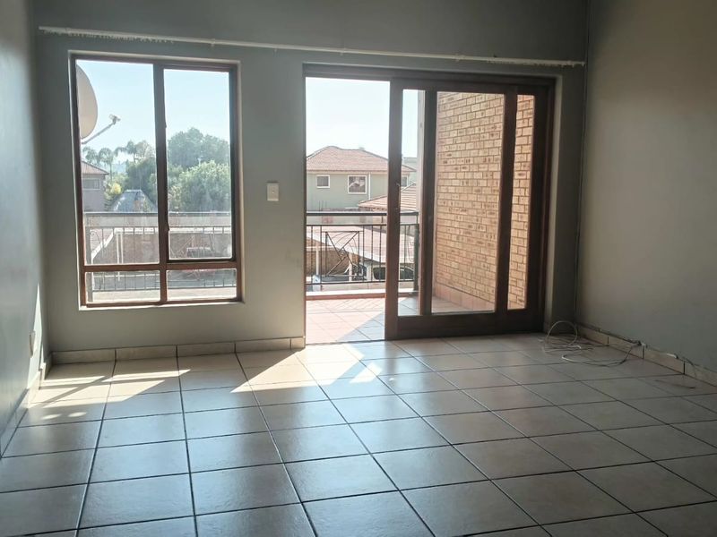 An empty living room featuring tiled flooring, large windows, and a sliding glass door providing access to an outdoor balcony area.