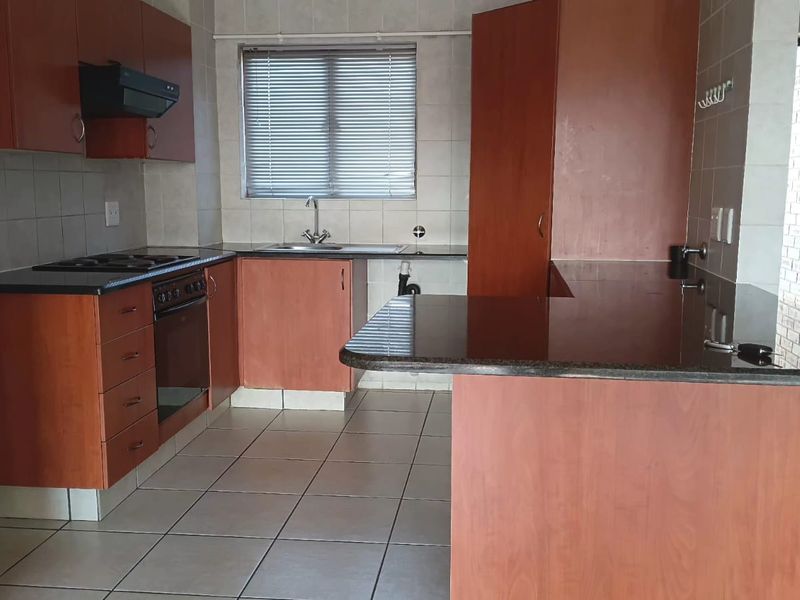 A functional kitchen featuring wood-finish cabinetry, granite countertops, built-in oven and hob, and tiled flooring with a breakfast bar area.