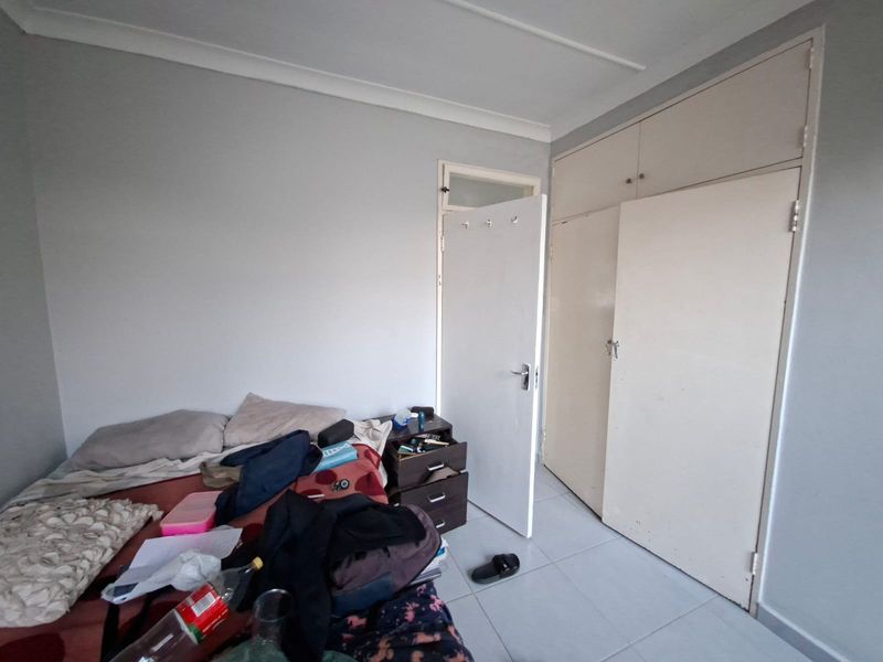 A bedroom featuring tiled flooring, built-in cupboards with overhead storage, and neutral wall finishes.