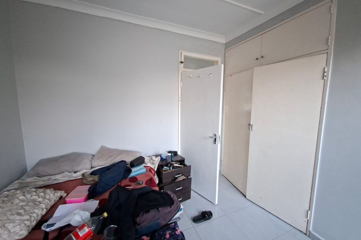 A bedroom featuring tiled flooring, built-in cupboards with overhead storage, and neutral wall finishes.